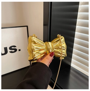 Close-up of golden bow-shaped evening bag with metallic chain and pleated texture
