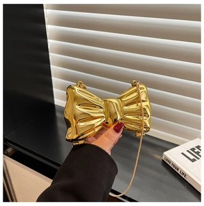 Close-up of a metallic gold bow-shaped evening clutch bag with a fine chain strap