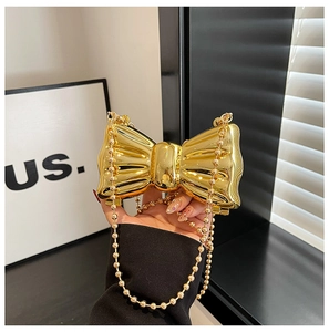 Close-up of golden bow-shaped metal evening bag with glossy finish and beaded chain strap