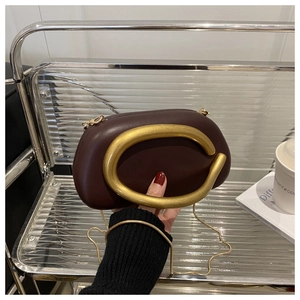 Close-up of burgundy leather clutch featuring a bold gold C-shaped handle and chain strap