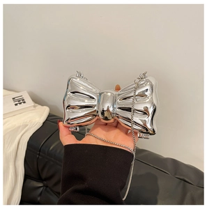 Close-up of a silver bow-shaped hard-shell evening clutch with a metallic chain strap
