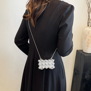 Mini silver metallic chain bag with spherical beads worn on a black dress