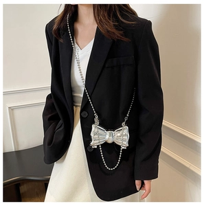 Close-up of a silver bow-shaped hard shell mini bag with metal bead chain on a black suit