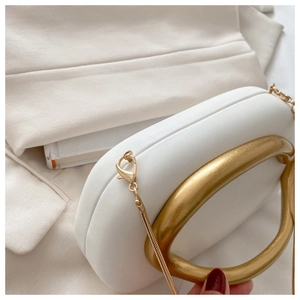 Close-up of white leather evening clutch with gold oval handle and fine chain strap