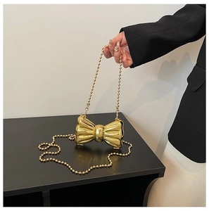 Close-up of golden metal bow evening clutch with mirror finish and beaded chain strap