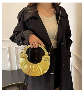 Detailansicht einer goldenen Abendtasche mit Rillenstruktur, Metallgriff und feiner Kette
