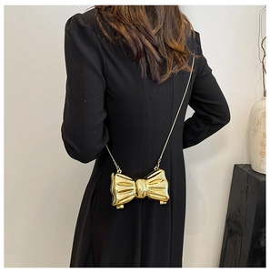 Mini golden bow-shaped evening bag with metal chain shown on model with black dress