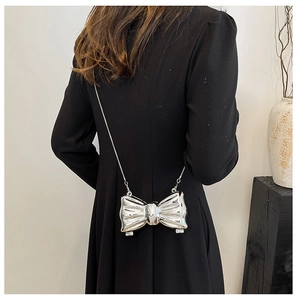 Detail of silver bow-shaped metal chain bag with high-shine mirror finish on black dress