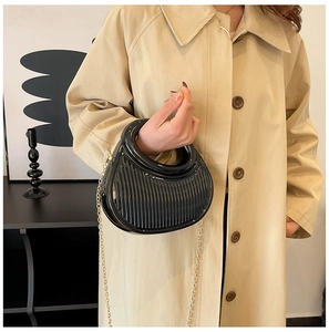 Detail of black glossy pleated crescent bag with circular handle and gold chain