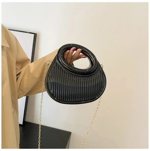 Detail of black pleated evening bag with round hollow handle and gold chain strap