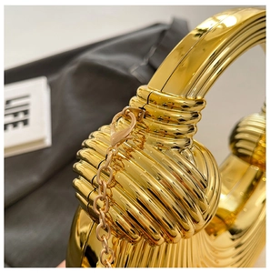 Detailansicht der goldenen Clutch mit Spiralrippen, Metallgriff und Ketten-Schulterriemen