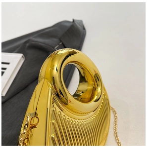 Close-up of golden evening bag with ribbed metal texture and integrated round handle