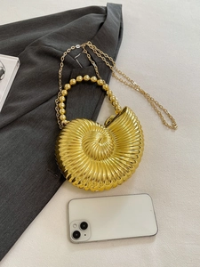 Detail of golden conch evening bag with spiral texture and beaded handle next to a phone