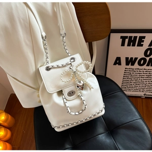 Detail of white leather mini backpack with pearl bow charm and silver chain strap