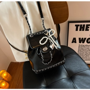 Detail of black glossy leather backpack with silver chain and pearl bow pendant charms