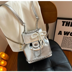 Close-up of silver chain detail and pearl bow pendant on a glossy metallic backpack