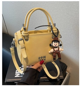 Detail of yellow leather bucket bag with metal logo and cute cartoon charm accessory