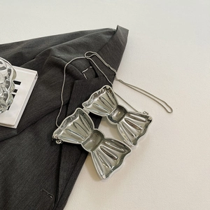 Mini silver bow-shaped metal evening bag with chain strap on a grey blazer