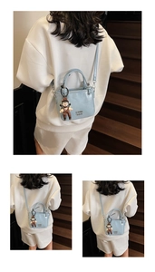 Detail of light blue oil wax leather bucket bag with cute doll charm and embossed text