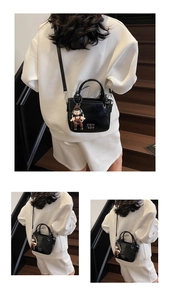 Detail view of a black leather bucket bag with metal logo and cute cartoon charm