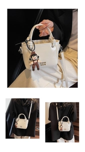 Detail of cream leather bucket bag featuring gold logo and cute boy charm accessory