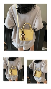 Detail of yellow bucket bag with doll pendant and COIN 2DH text on matte PU leather
