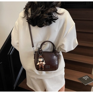 Detail view of small dark brown bucket bag with cute cartoon doll and metal logo detail
