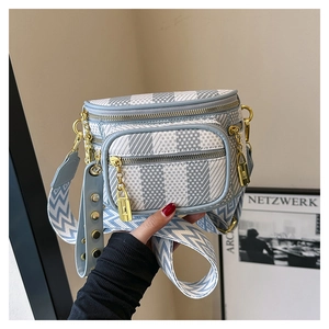 Close-up of geometric striped saddle bag with gold hardware and wide woven strap