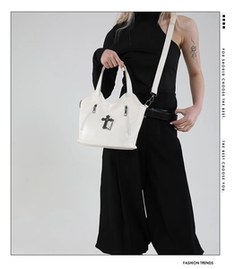 Detail of white cross pendant and metallic zippers on lychee texture leather bag