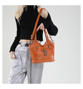 Close-up of orange litchi-textured tote bag featuring a vintage metal cross pendant