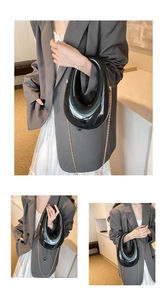 Detail of glossy black acrylic U-shaped handbag with a slim golden metal chain strap
