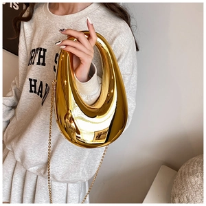 Macro detail of glossy gold acrylic shell bag with metallic chain and mirror finish
