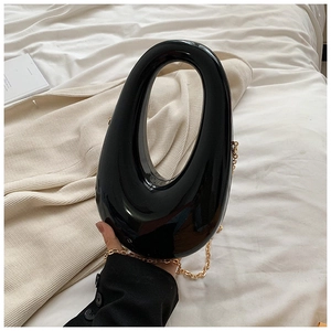 Close-up of black glossy acrylic box bag with unique oval cutout handle and gold chain strap