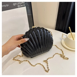 Close-up of shell-shaped acrylic evening bag with glossy black finish and gold chain