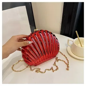 Detail of red shell-shaped evening clutch bag with golden chain strap on white desk