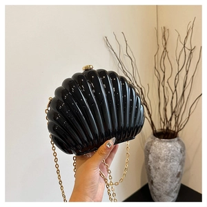 Close-up of black shell-shaped acrylic clutch bag with glossy finish and gold chain