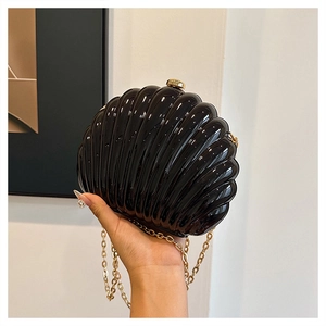 Close-up of black shell-shaped acrylic clutch with glossy texture and gold chain strap