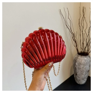 Close-up of bright red shell-shaped evening bag with gold chain and round knob clasp
