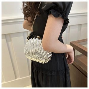 Detail of silver shell-shaped clutch with gold chain strap on a model's shoulder