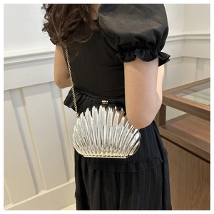 Silver shell-shaped clutch bag with metal chain strap shown worn with a black dress