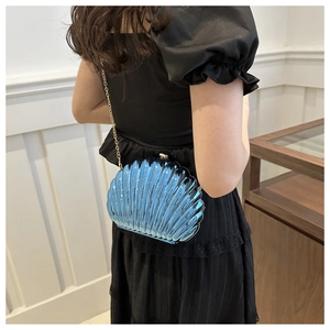 Blue shell-shaped acrylic evening clutch bag with gold chain strap shown on model
