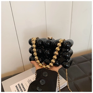 Detail of glossy black acrylic spherical clutch bag with chunky gold beaded chain strap