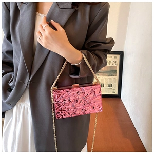 Dettaglio macro della borsa clutch in acrilico rosa acceso con catene dorate