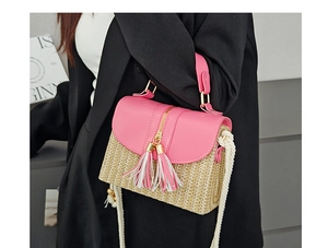 Détail du rabat en cuir rose et de la paille tressée avec pompon sur le sac de plage