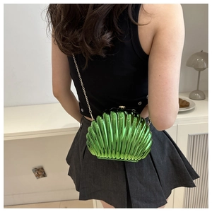 Detail of metallic green shell-shaped clutch bag with golden chain strap on a model