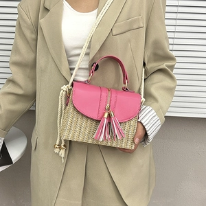 Détail d'un sac en paille avec rabat en cuir rose, pompon à franges et bandoulière