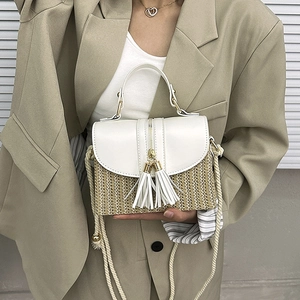 Détail du sac en paille tissée avec bordure en cuir blanc, zip doré et accents de pompons