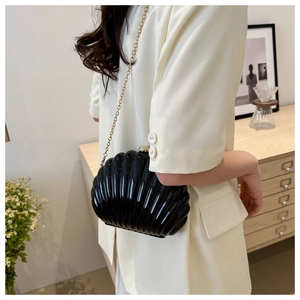 Detail of black acrylic shell clutch bag with gold chain strap on stylish woman