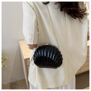 Detail of a black glossy shell clutch bag featuring a golden chain and ribbed texture