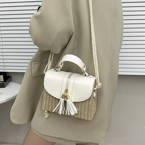 Détail du sac bandoulière en paille avec rabat en cuir blanc et gland sur un modèle